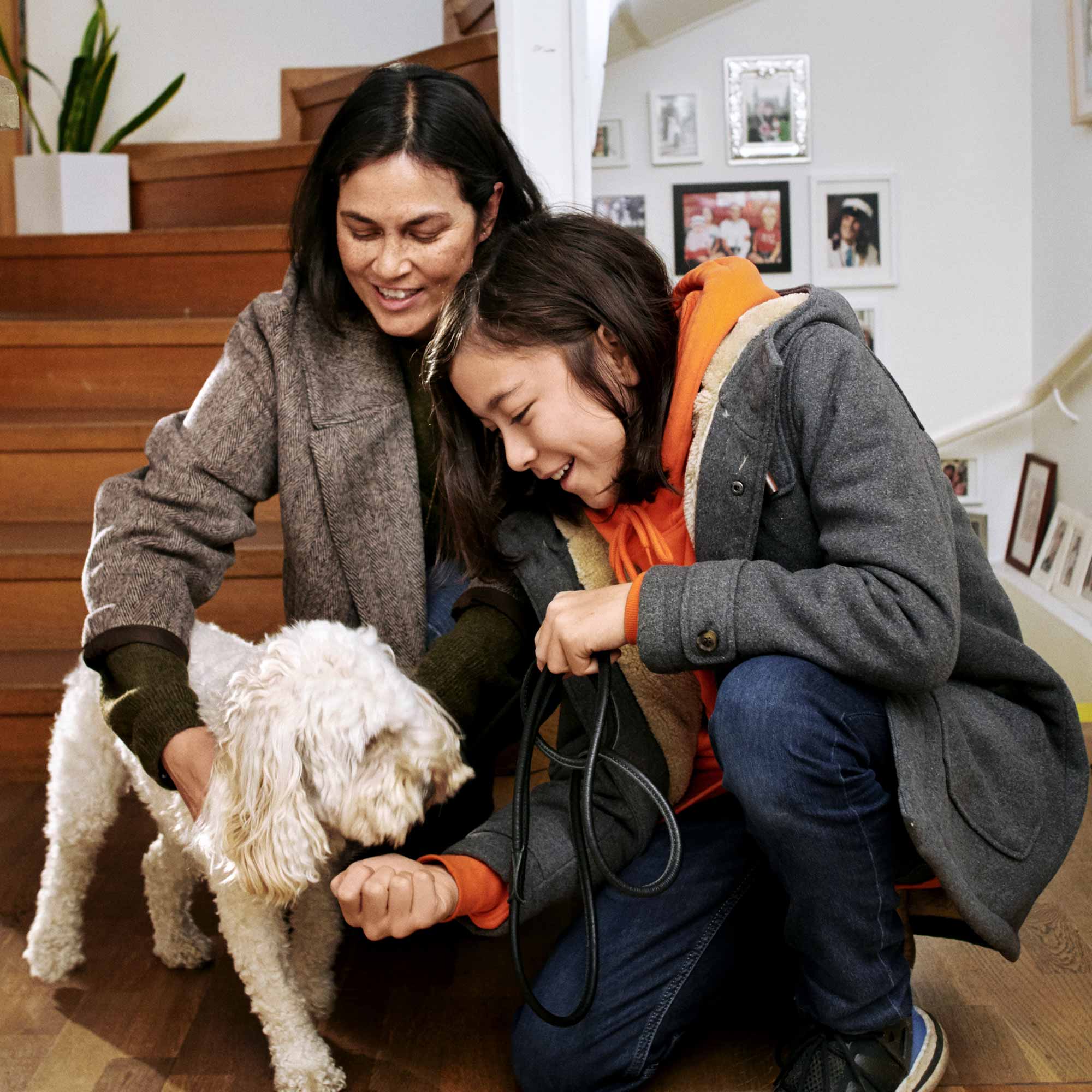 Mamma och tonåring klappar familjens hund i hallen