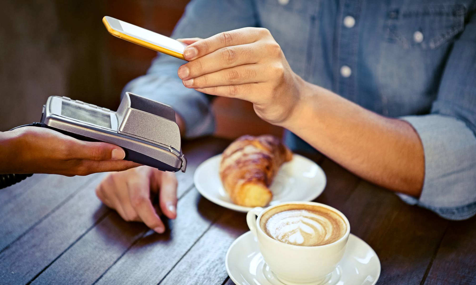 Person på ett café betalar med mobilen.